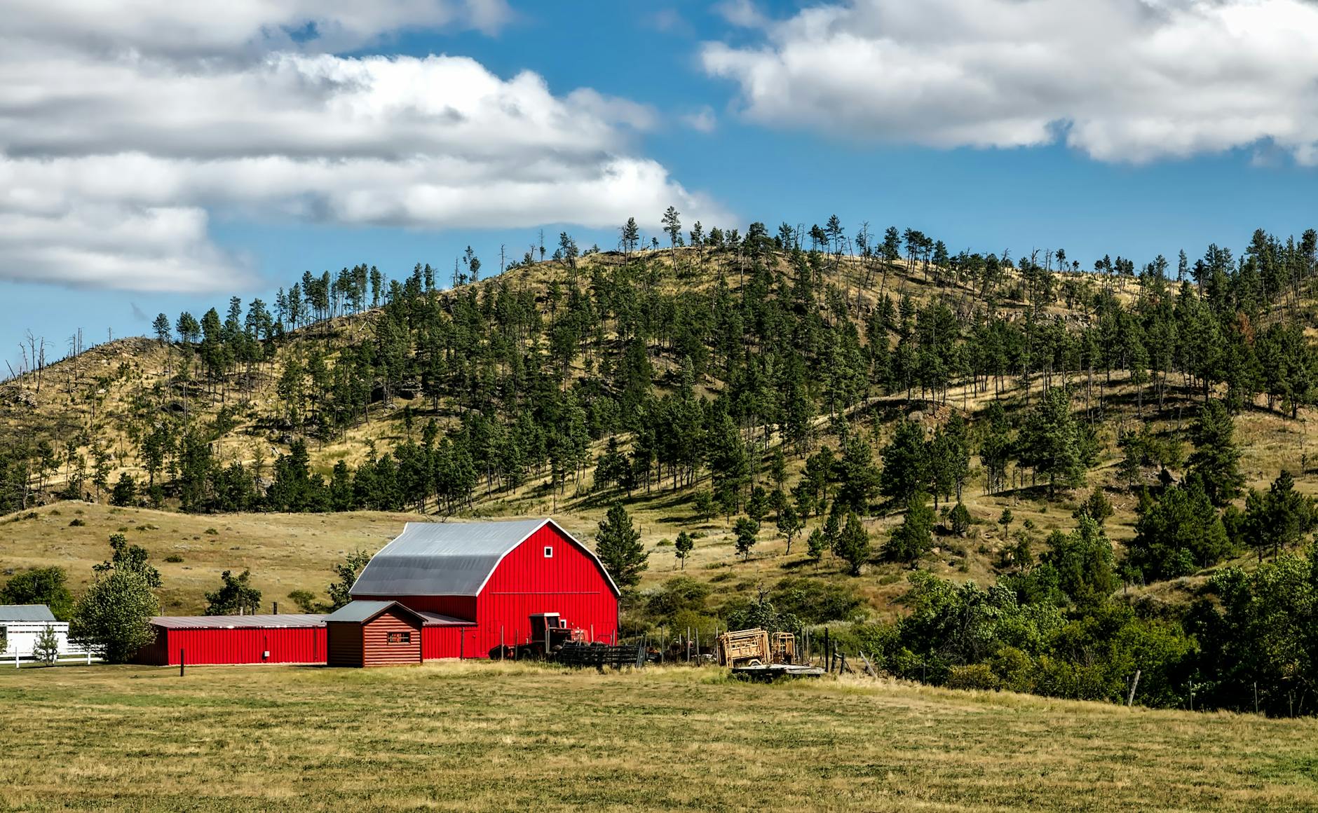 Picturesque red barn surrounded by rolling hills and pine trees under a cloudy sky.