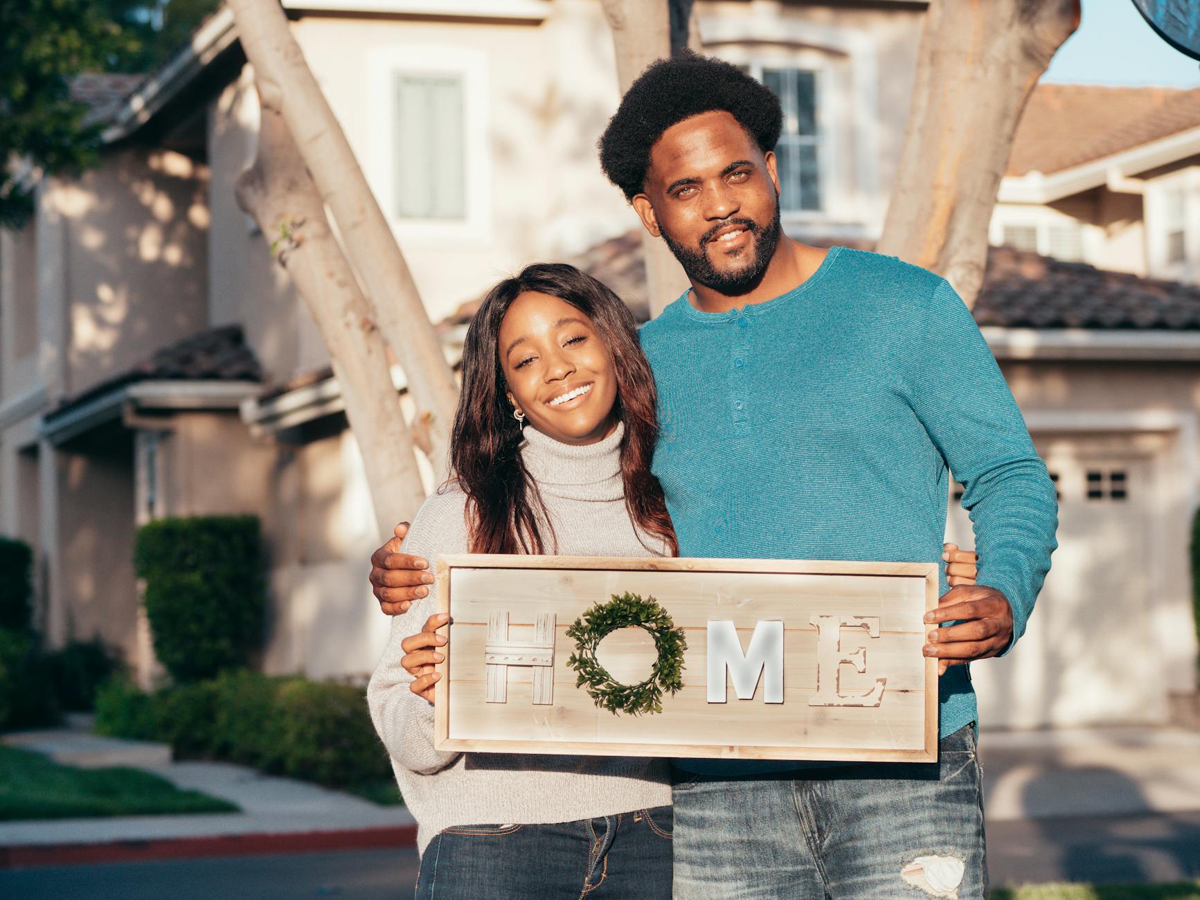 Happy couple joyfully holding a 'Home' sign in front of their new house.