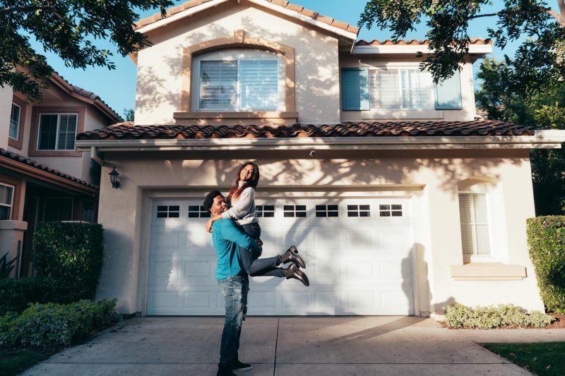 A joyful couple smiling and embracing in front of their new home on a sunny day.