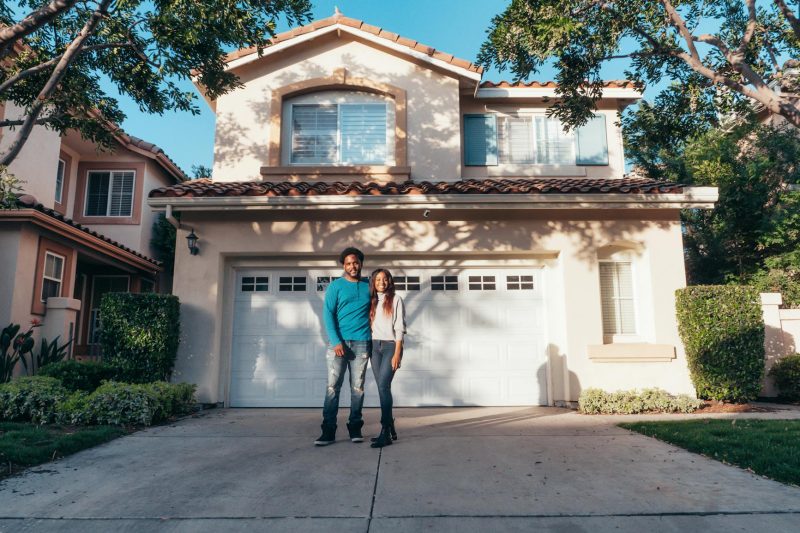 Smiling couple outside their new home, enjoying a sunny day.