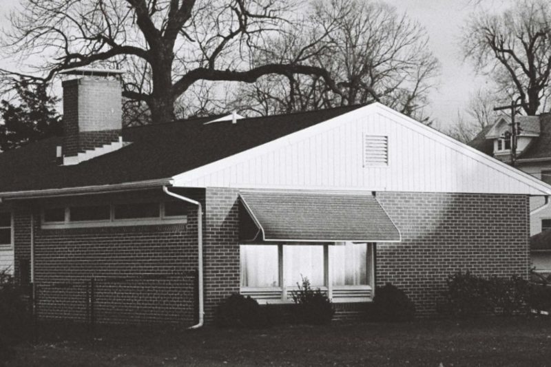 Classic brick house blanketed in snow, surrounded by leafless trees in a winter scene.