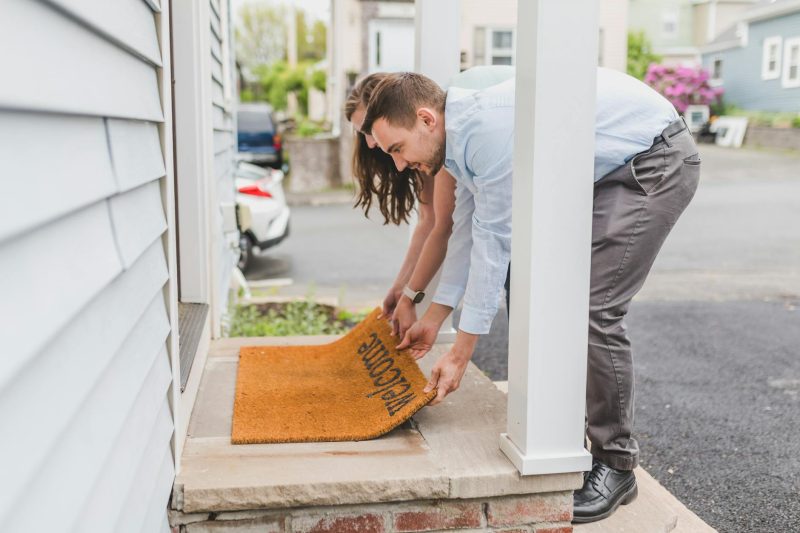 A young couple placing a welcome mat on their new home's porch, celebrating a fresh start.