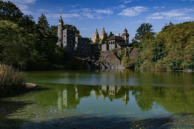 Belvedere Castle in Central Park reflecting in the water, surrounded by lush greenery and tranquil scenery.