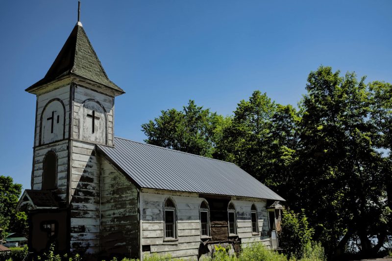 Weathered wooden chapel surrounded by lush trees in a rural setting in Redfield, NY.