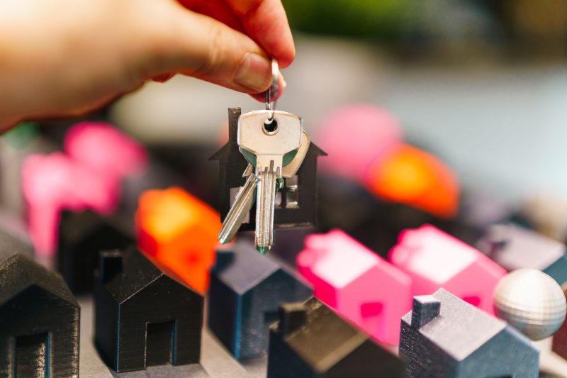 Colorful miniature houses and a hand holding keys, symbolizing real estate choices.