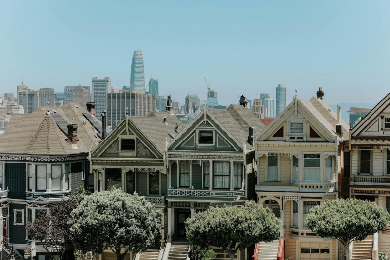 Colorful Victorian houses in San Francisco with a distant city skyline backdrop on a clear day.