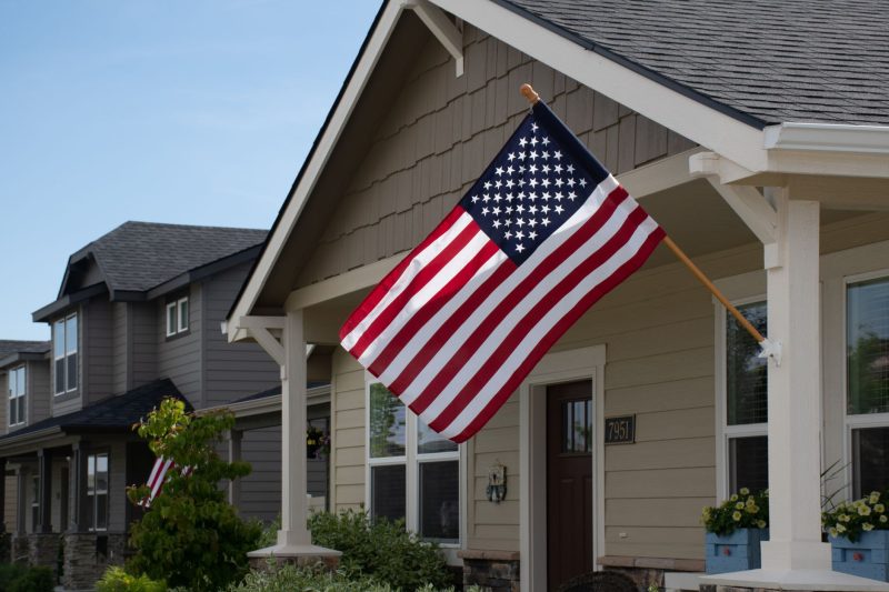 A vibrant American flag waves in front of a stylish suburban house under clear daylight.